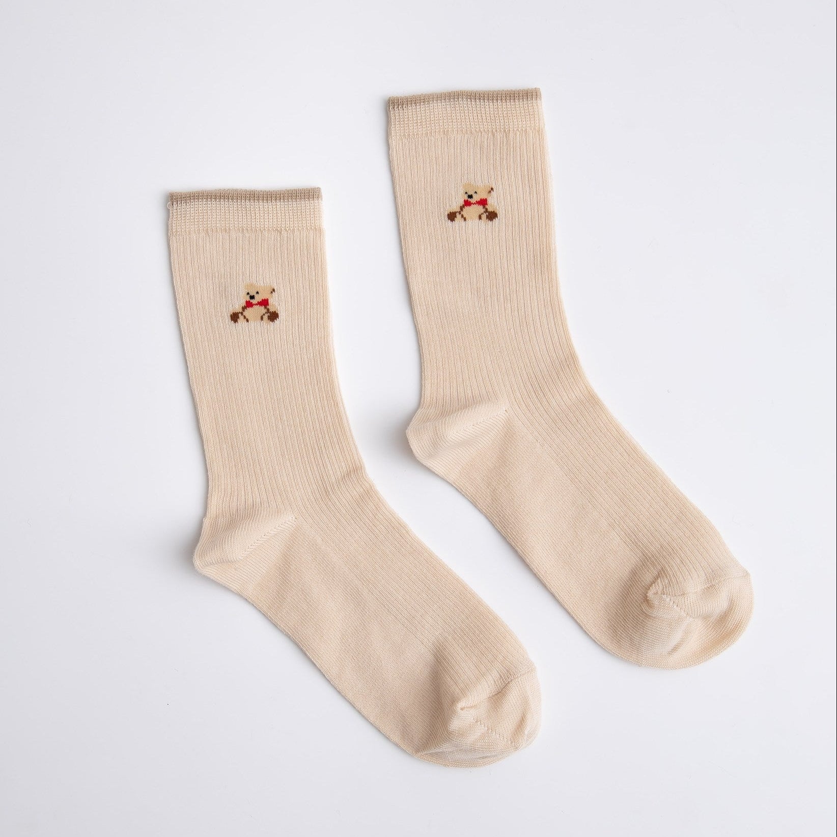 Pair of beige socks with small embroidered designs on a light gray background

